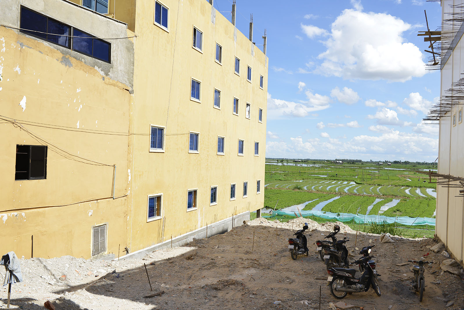 This land in Phnom Penh, Cambodia is available for sale, with buildings on both sides and farmland behind it.